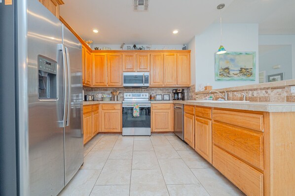 A modern kitchen with wooden cabinets, stainless steel appliances, and a tiled floor.