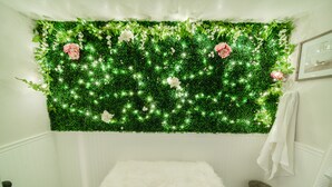 Une salle de bain avec un mur recouvert de plantes vertes, un banc moelleux blanc et un porte-serviettes blanc.