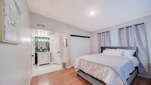 Une chambre à coucher comprenant un lit, une commode, un miroir et une porte donnant sur une autre pièce.
