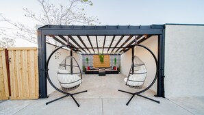 Un espace extérieur aménagé, abrité, avec deux fauteuils suspendus et un canapé.