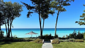 A pathway leading to a beach with a striped umbrella, surrounded by trees and a clear view of the ocean.