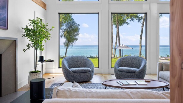A modern room with large windows, two grey armchairs, a small table, and a potted plant.
