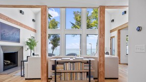 A modern living room with a fireplace, a bookshelf, and a large window overlooking a body of water.