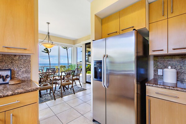 Una cocina con armarios de madera, un refrigerador de acero inoxidable y un comedor con vista al océano.