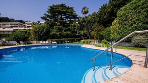 Ein klares, blaues Schwimmbecken mit Stufen, umgeben von Grünpflanzen und einem Gebäude im Hintergrund.