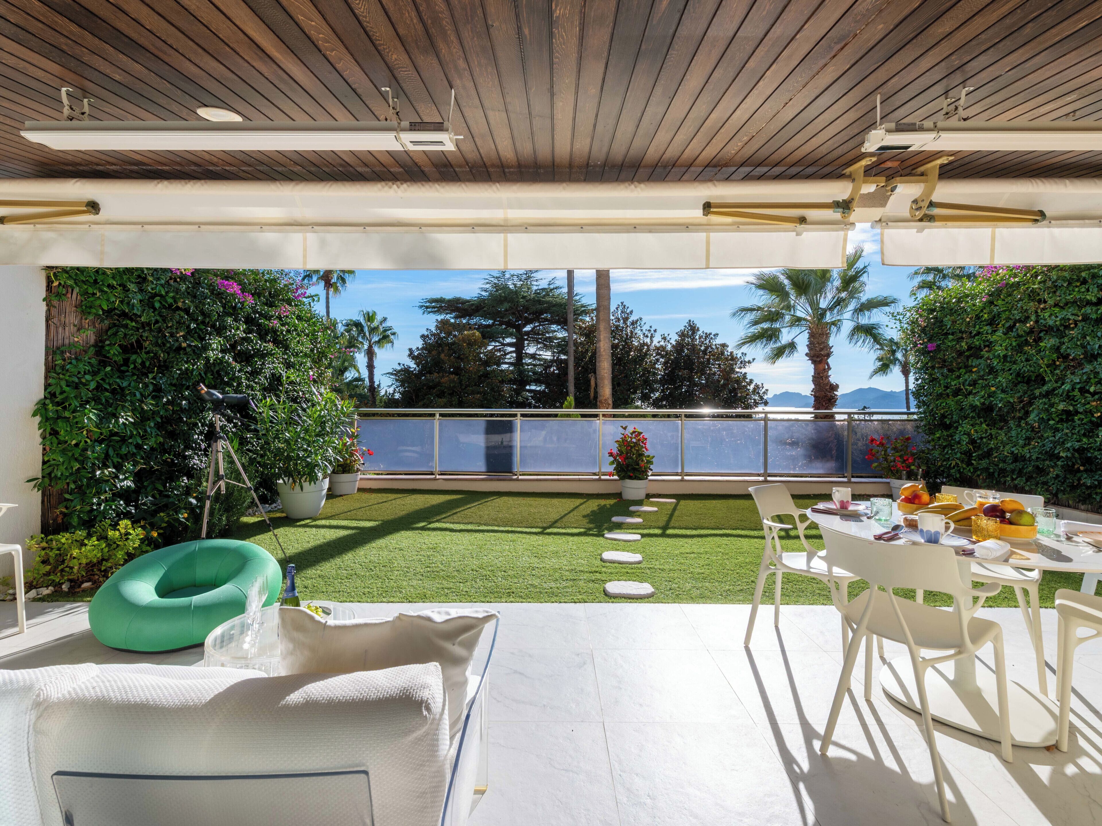 Een modern buitenpatio met een eettafel voor twee personen, omringd door weelderige beplanting en een helder uitzicht op de oceaan.