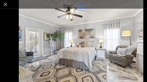 A bedroom with a bed, a chair, a nightstand, a lamp, a ceiling fan, and a patterned rug.