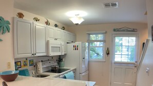 A kitchen with white cabinets, a central island, and a dining area with wicker chairs. - Poolside Paradise in Key West Golf Club (Key West)