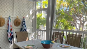 A dining area with a table set for four, surrounded by chairs, a ceiling fan, and a view of palm trees through large windows. - Poolside Paradise in Key West Golf Club (Key West)