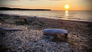 Ein Kiesstrand mit einem großen Felsen im Vordergrund und einem Sonnenuntergang im Hintergrund.