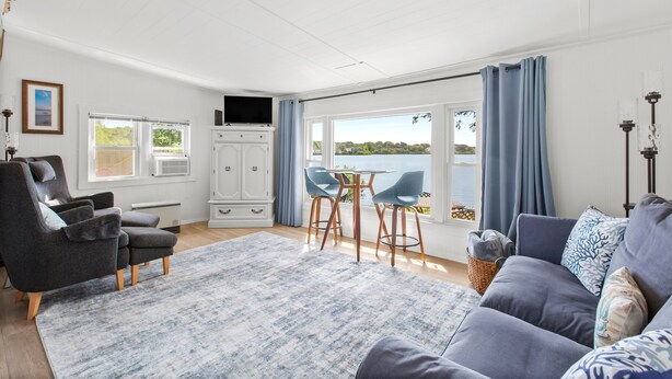 Ein modernes Wohnzimmer mit einem grauen Sofa, einem blauen Teppich mit Muster und einem Essbereich mit zwei Stühlen und einem Tisch.
