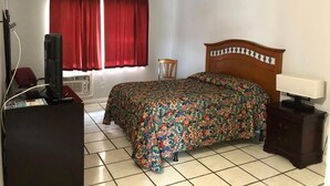 Een slaapkamer met een bed, een bureau met een computer, een stoel en een raam met rode gordijnen.