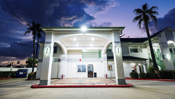 A hotel entrance with a covered walkway, palm trees, and a clear sky. - Palace Inn I10East & John Ralston (Houston)