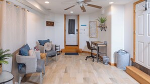 Un salon comprenant un canapé, une table basse, un bureau et un ventilateur de plafond.