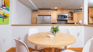 Une cuisine moderne avec des meubles en bois, des appareils électroménagers en acier inoxydable et une table de salle à manger ronde en bois, assortie de chaises blanches.