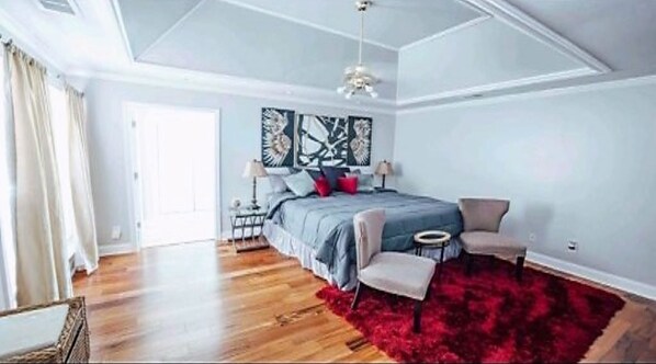 A spacious bedroom with a large bed, a red rug, and a modern chandelier.
