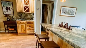 A kitchen with wooden cabinets, a stone backsplash, and a bar area with stools. - Blue Knob Big Snow Condo  (Claysburg)