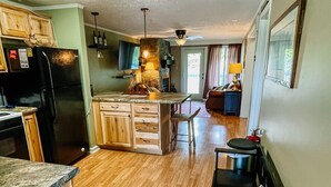 A kitchen with wooden cabinets, a black refrigerator, a marble countertop, and a dining area with a bench and chairs. - Blue Knob Big Snow Condo  (Claysburg)