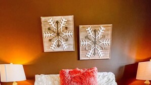 A bedroom with a large bed, two wall-mounted lamps, and two snowflake wall art pieces. - Blue Knob Big Snow Condo  (Claysburg)