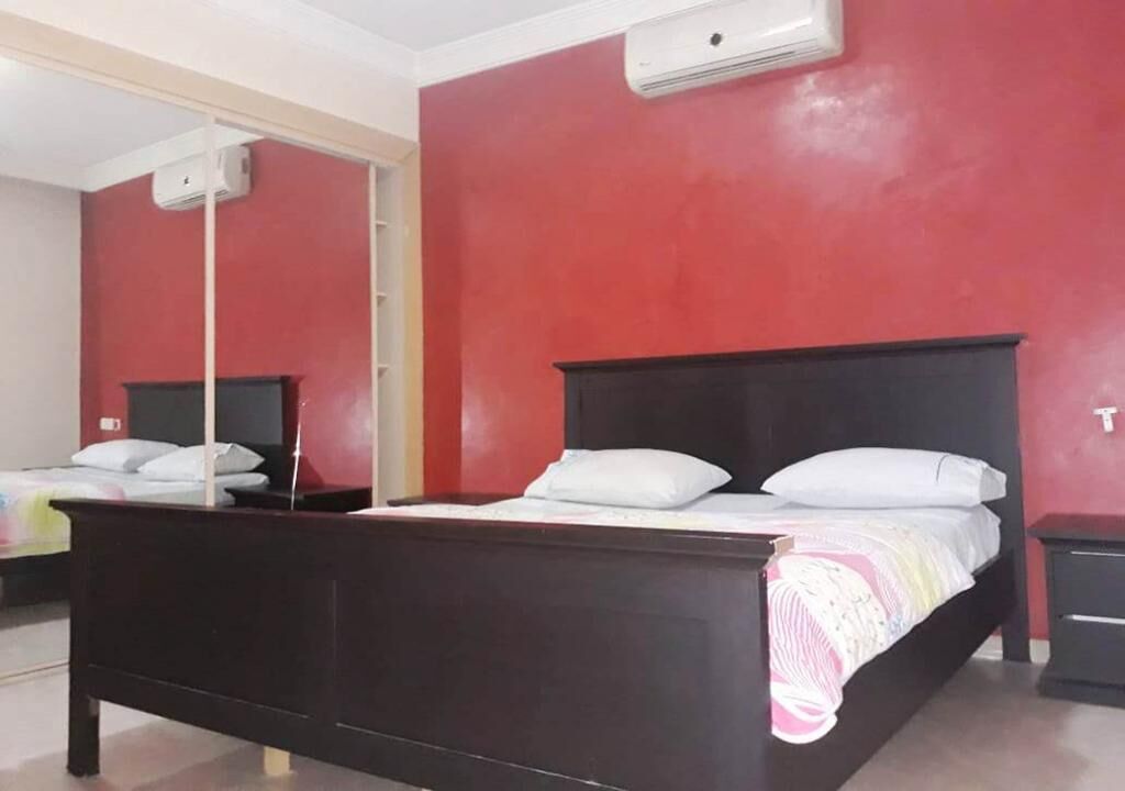 A bedroom with a wooden bed, a red wall, and a white air conditioning unit.