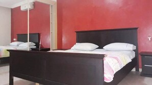 Un dormitorio con una cama de madera, una pared roja y un equipo de aire acondicionado blanco.