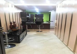 Ein schmales Entree mit einer Küchenzeile, die einen Kühlschrank, eine Mikrowelle und eine Kaffeemaschine beinhaltet. Zwei Barhocker und ein kleiner Tisch mit Dekorationen sind ebenfalls vorhanden. Die Wände sind verkleidet und der Boden ist mit Fliesen belegt.
