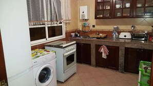 Une cuisine compacte équipée d’un lave-linge, d’un four et d’un petit plan de travail sur lequel se trouvent un grille-pain et un distributeur d’eau.
