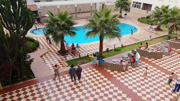 Une cour avec une piscine, des palmiers et un sol à carreaux.