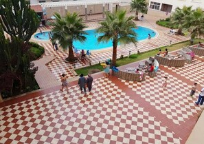 A courtyard with a pool, palm trees, and checkered flooring. - Beautiful Apartment in Arena Martil 5181 (Martil)