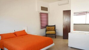 A bedroom with a bed, a chair, a dresser, and a window with blinds.