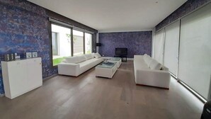 A modern living room with a white sofa set, a glass coffee table, and a flat-screen TV.