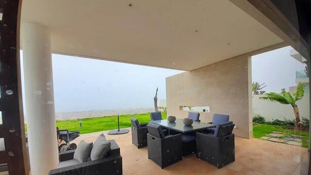 An outdoor patio with a dining area, a sofa, and a view of the sea.