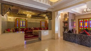Ein luxuriöses Interieur mit aufwendigen Deckenornamenten, einer Sitzecke mit Kissen und einer Kristallleuchter.