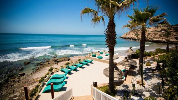 A beach resort with lounge chairs, palm trees, and a view of the ocean. - Residence La Source Taghazout 5217 (Taghazout)
