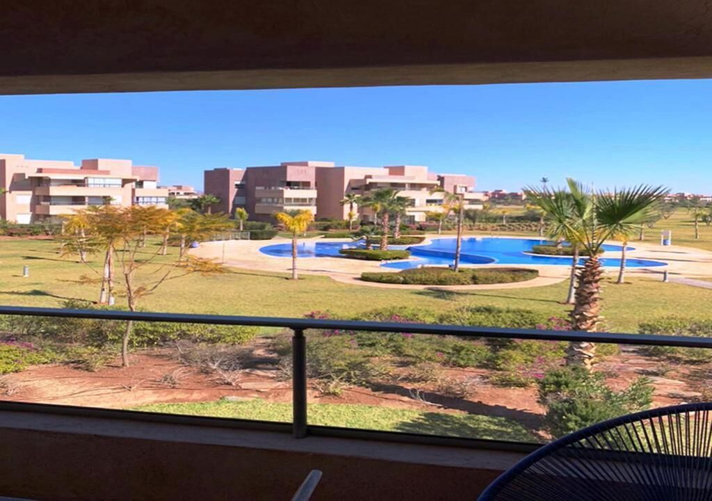Blick auf ein Hotel mit mehreren Gebäuden, einem Poolbereich und einem Balkon mit einem Stuhl.