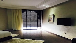 Habitación de hotel con una cama grande, un televisor de pantalla plana en la pared y un ventanal con persianas.