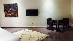 Habitación de hotel con cama, televisor montado en la pared, una pequeña mesa con dos sillas y un cuadro abstracto colorido en la pared.