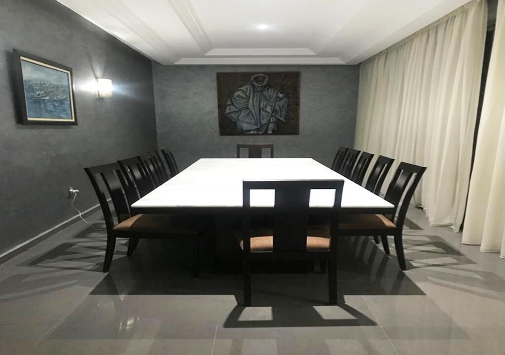 A conference room with a long table and chairs, a painting on the wall, and a light fixture.