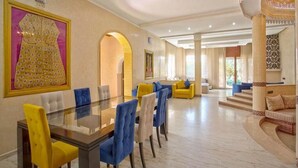A spacious dining area with a glass table and chairs, a large framed artwork on the wall, and a grand staircase leading to a balcony. - High standing villa with swimming pool 5231 (Marrakech)