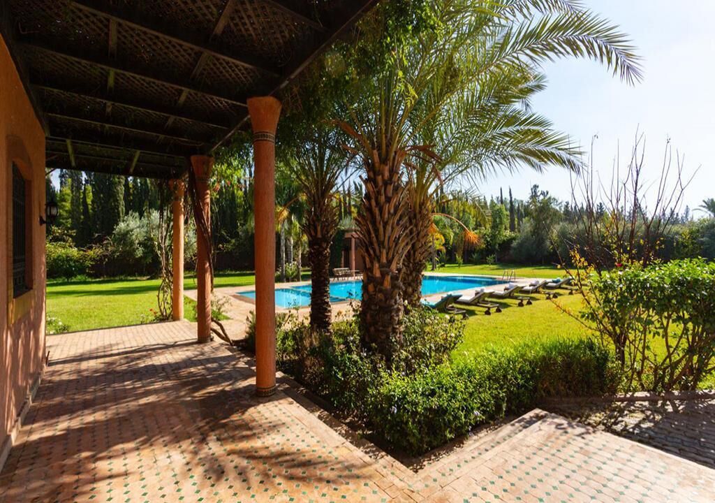 A covered outdoor area with a pool, palm trees, and a well-maintained lawn.