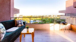 A balcony with a sofa, a small table, and a chair. The balcony overlooks a pool and greenery. - Splendid apartment in Prestigia Marrakech 5234 (Marrakech)