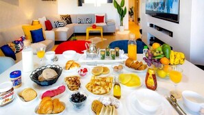 A breakfast buffet with various pastries, fruits, and beverages on a table in a modern living room with a sofa and a TV in the background. - Splendid apartment in Prestigia Marrakech 5234 (Marrakech)