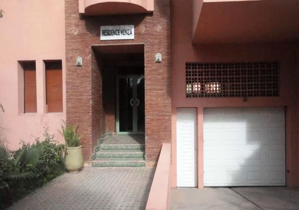 A building entrance with a sign reading "RESIDENCE KENZA," a brick facade, a covered entrance, and a garage with two white doors.