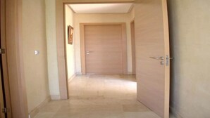 Un pasillo con una puerta de madera al final, un interruptor de luz en la pared y un cuadro enmarcado a la izquierda.