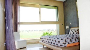 Un dormitorio con cama, una silla y un ventanal con vistas a un paisaje verde.