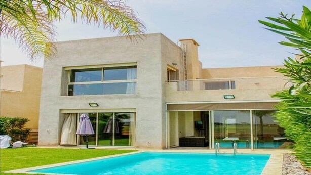 Una casa moderna de dos pisos con piscina, ventanas amplias y un porche cubierto.