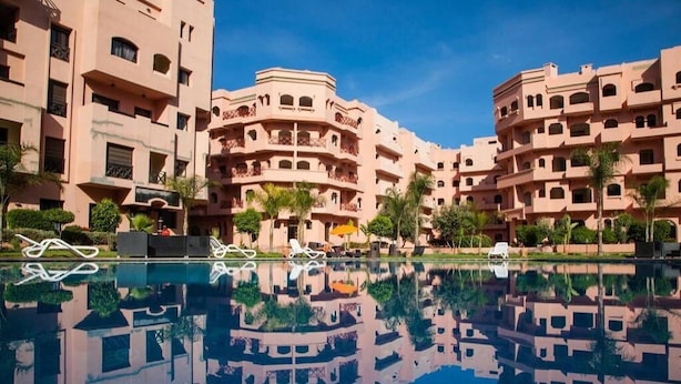 A hotel with multiple balconies, a swimming pool, and palm trees. - Pleasant apartment in Premium Village Marrakech 5239 (Marrakech)