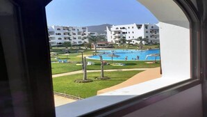 Une vue d’un espace piscine avec une piscine, des palmiers et un bâtiment en arrière-plan.