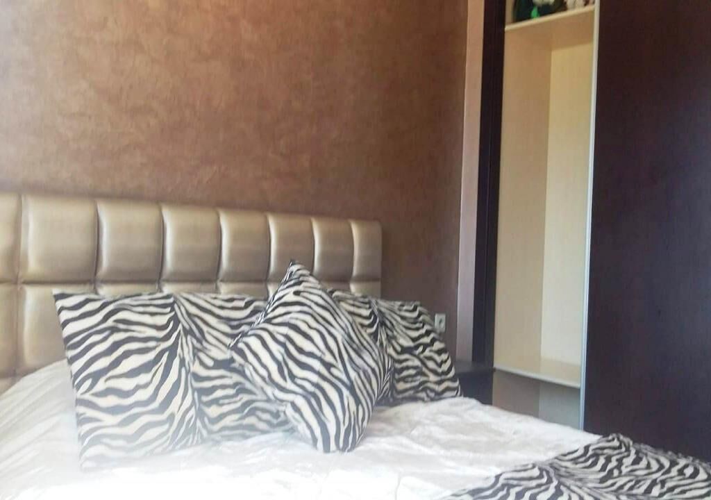 Ein Schlafzimmer mit einem gesteppten Kopfteil, Kissen mit ZEBRA-Muster und einer Bettdecke in neutralen Farbtönen.