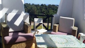Un balcon agrémenté de meubles en osier, une table recouverte d’une nappe à motifs floraux et une vue sur une zone boisée.